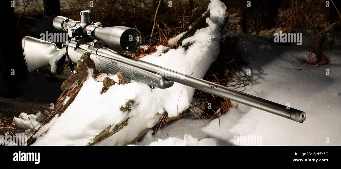 Large rifle scople and bolt action rifle on a snowy log in the forest Stock Photo