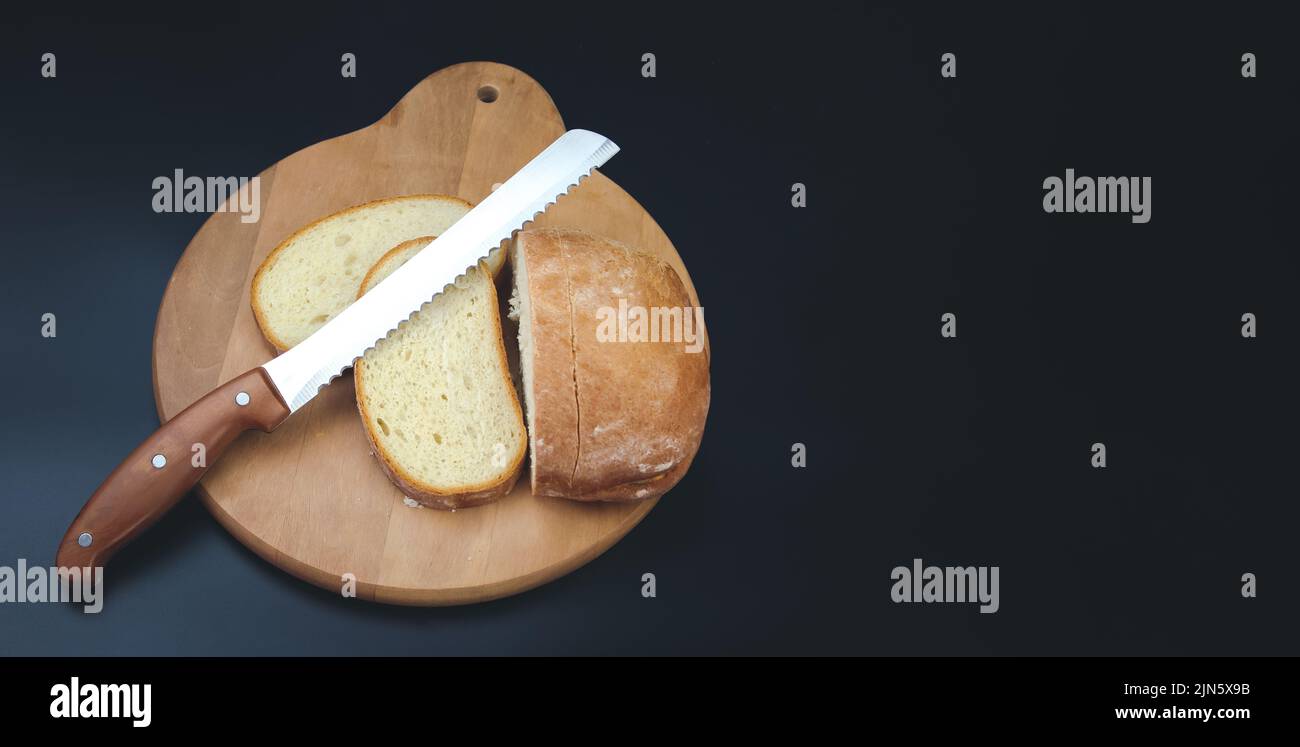 A large knife cuts thin pieces of white bread from a rectangular loaf Stock Photo