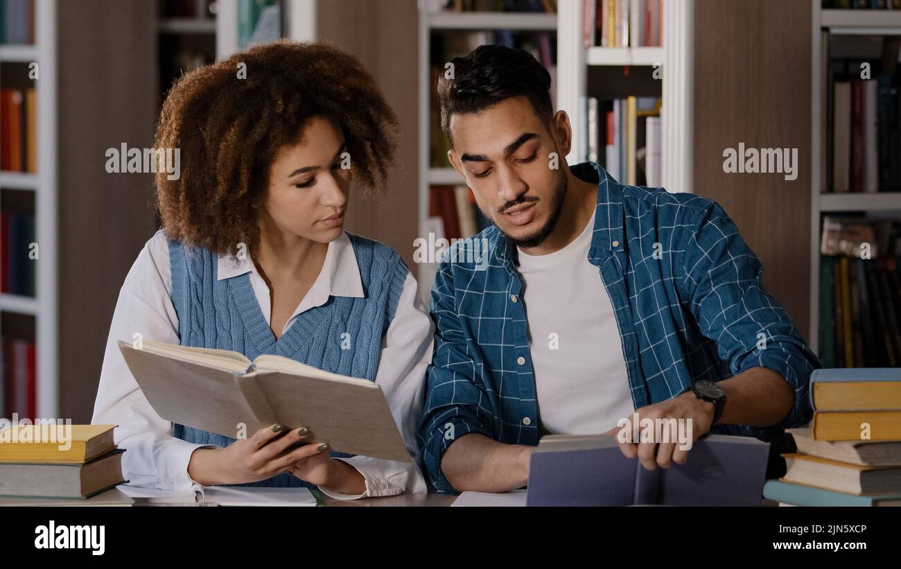 Two diverse students sitting in university library preparing for exam