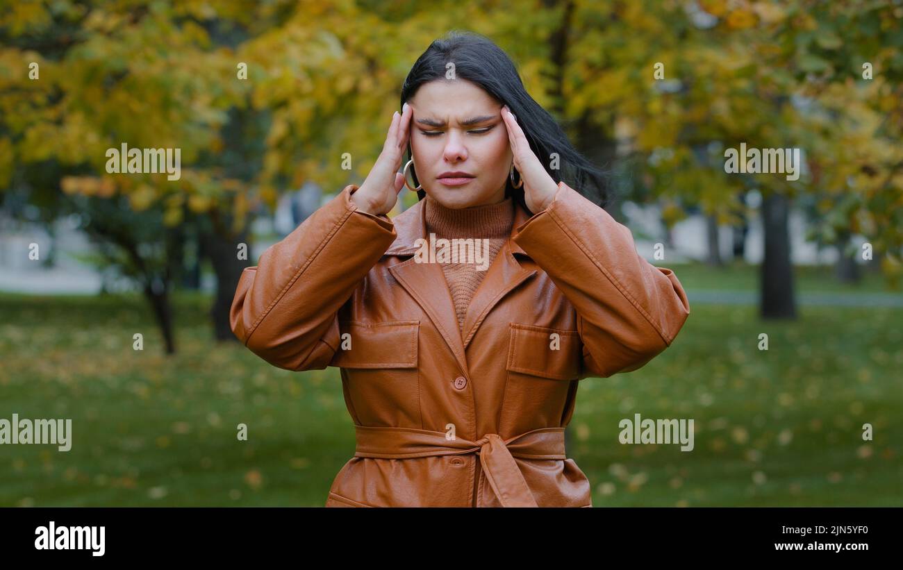 Closeup upset hispanic girl standing outdoors suffer from feeling unwell headache malaise soreness rubs temple agitated young woman worried about bad Stock Photo