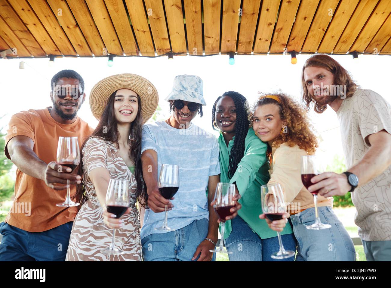 Waist up portrait of diverse group of friends looking at camera and holding wine glasses while enjoying outdoor party in Summer Stock Photo
