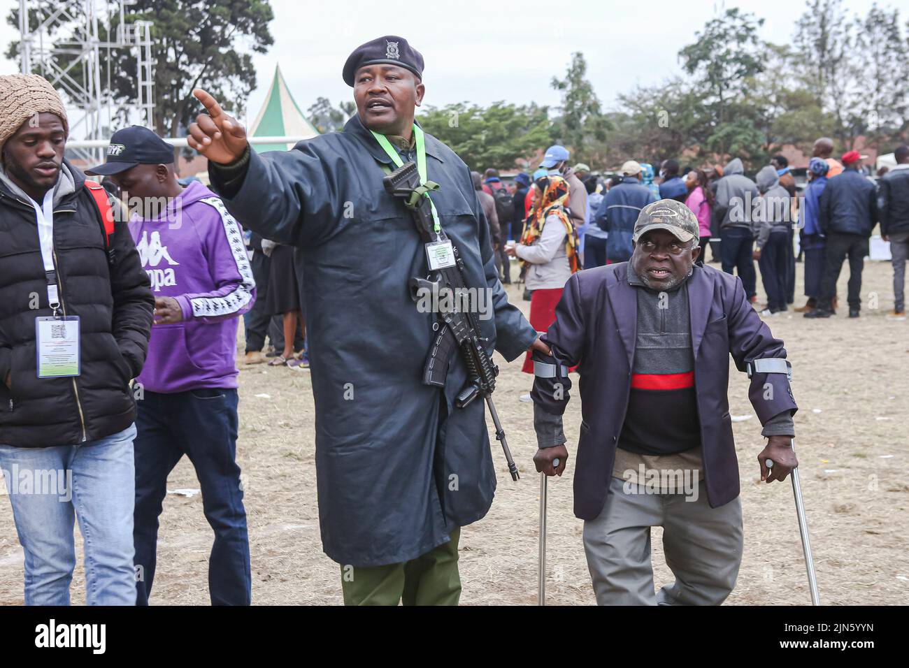 A Kenyan police officer helps a physically challenged Kenya man to locate his polling line, Kenya's general elections on 9th August 2022, at St. Teresa's Primary and Secondary school in Nairobi. Kenyan voters head to the polls. They will elect the president and deputy president, county governors and running mates, members of the Senate, representatives of the National Assembly (including women county representatives) and members of County Assemblies. This year, voting will be held across an estimated 46,232 polling stations. Stock Photo