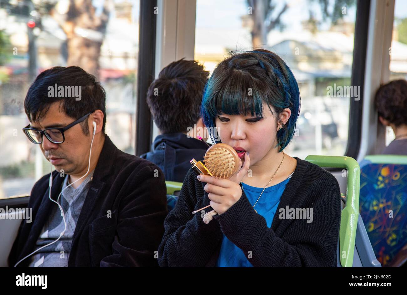 An Asian office worker does her makeup on the train while commuting to work in Melbourne, Australia Stock Photo
