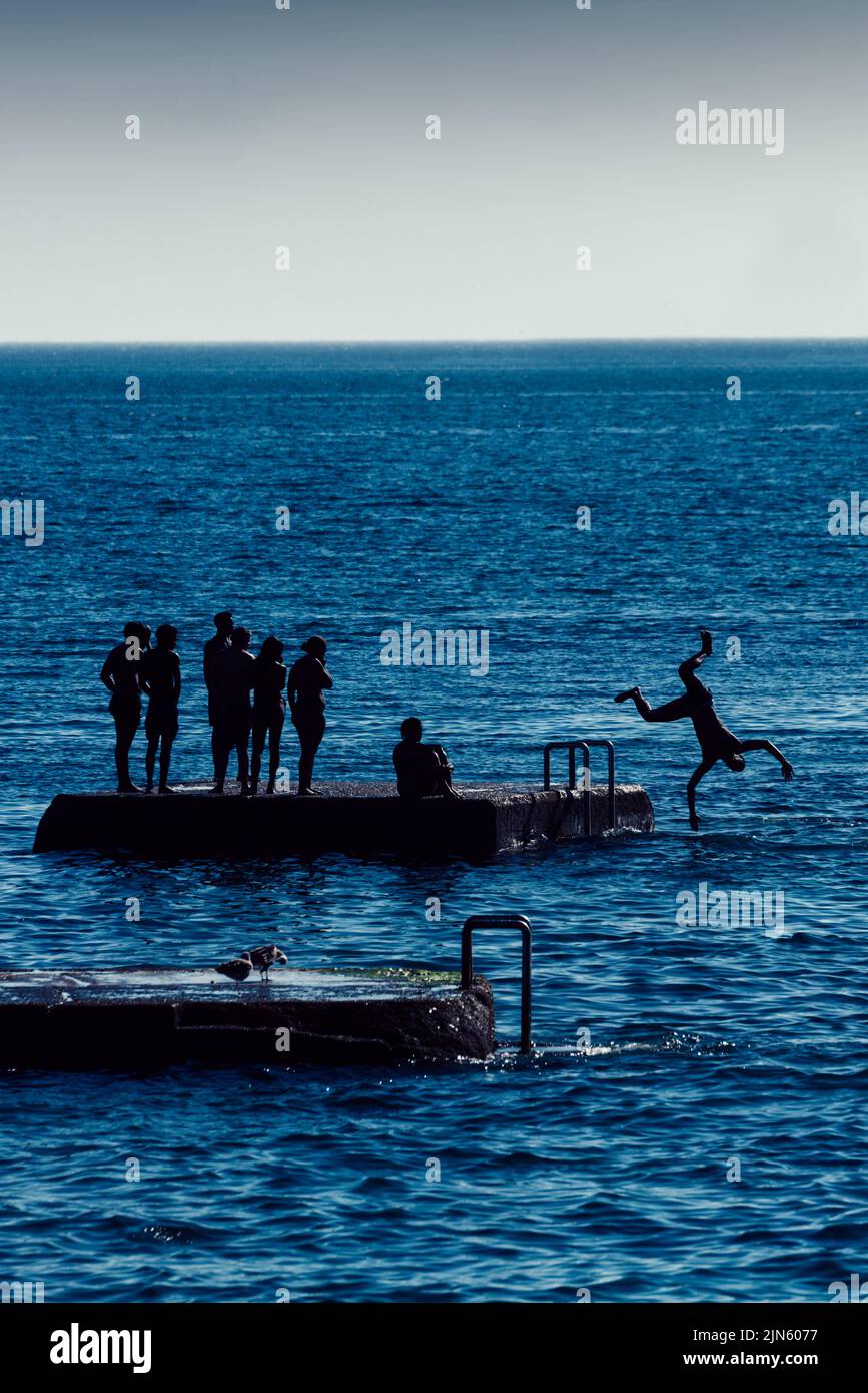Silhouette of teenagers playing on a concrete island at Tamariz beach in Estoril, Portugal on a summer day Stock Photo