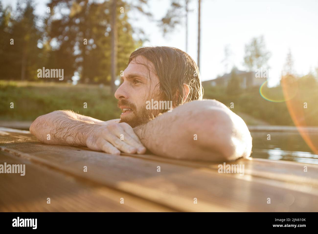 Portrait of handsome Caucasiahn man swimming in lake by pier with lens flare Stock Photo