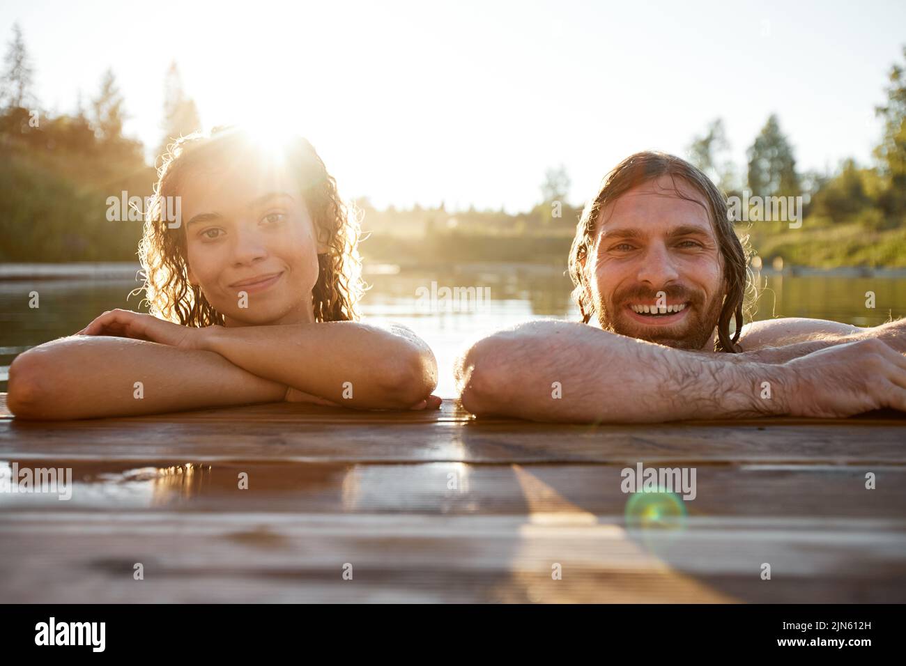Summer portrait of young couple swimming in lake lit by Sunlight and smiling Stock Photo