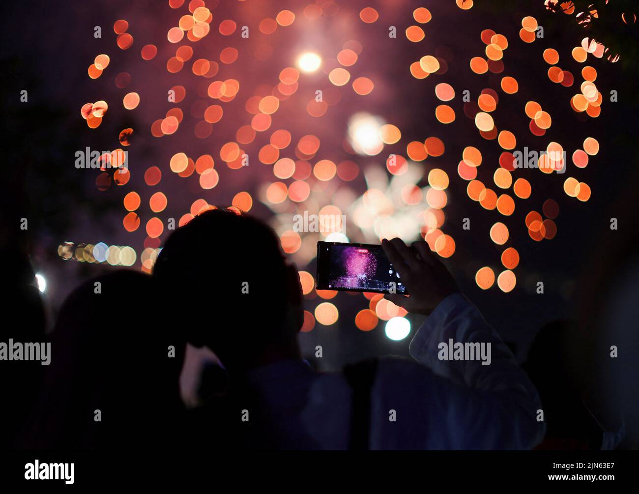 A couple films with their mobile phones as fireworks explode over Marina Bay during National Day celebrations in Singapore August 9, 2022. REUTERS/Edgar Su Stock Photo