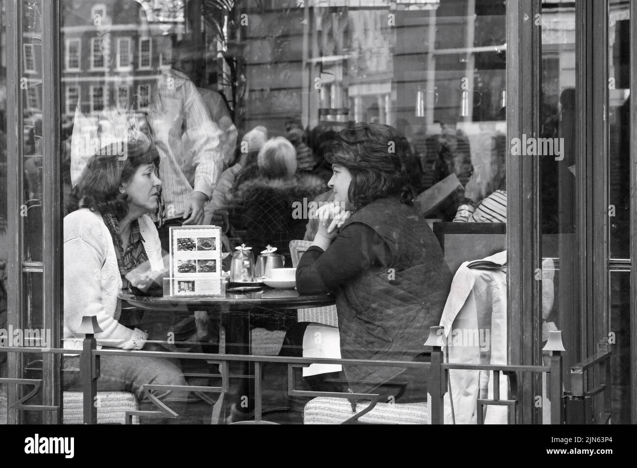 A cafe with reflections and two women seated at a table having a casual conversation and drinking tea, York, North Yorkshire, UK. Stock Photo