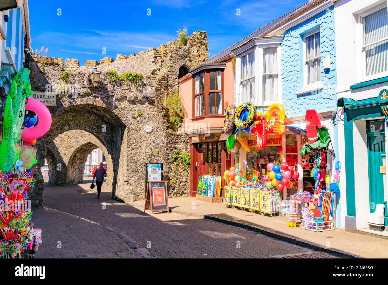 Colourful bucket and spade shops next to the historic old town walls at Five Arches in St George's Street, Tenby, Pembrokeshire, Wales, UK Stock Photo