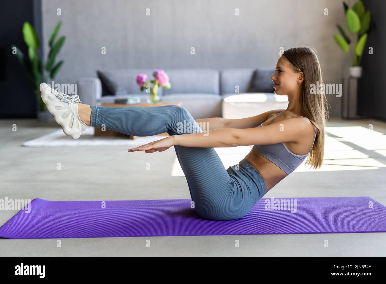 Attractive slim girl in sportswear is doing abs exercises on the floor at home Stock Photo