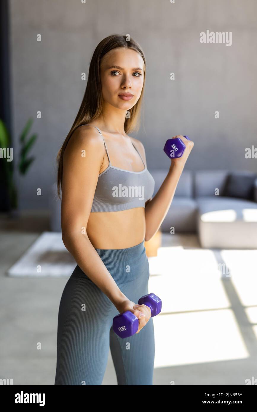 Woman exercising with dumbbells at home. Sporty beautiful woman exercising at home to stay fit. Stock Photo
