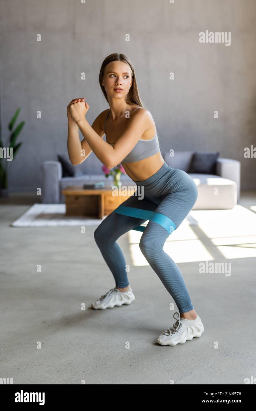 Sporty young woman exercising at home with rubber band. Healthy and sporty lifestyle. Pretty slim girl takes care about her health, does sit-ups . Stock Photo