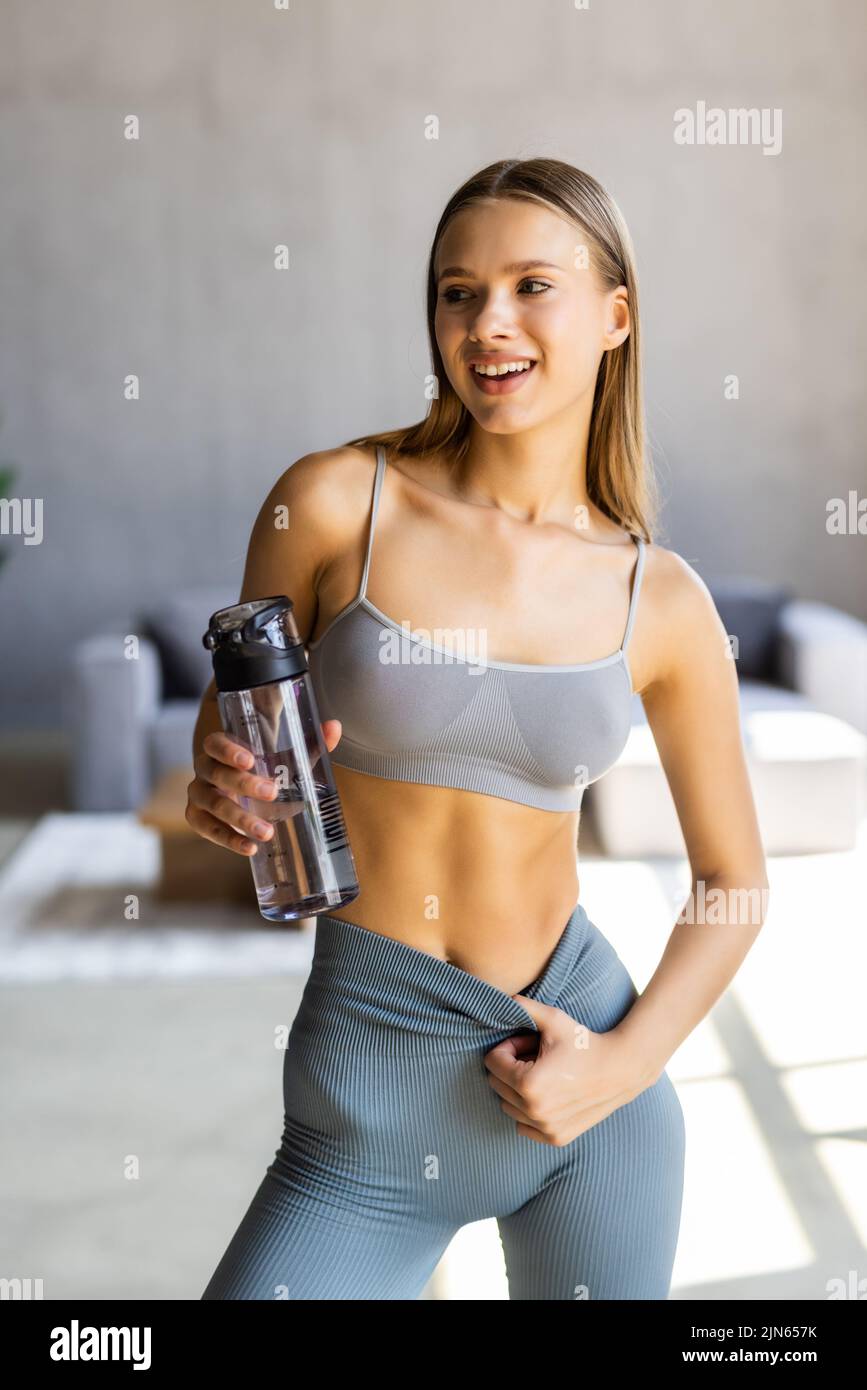 Beautiful woman drinks a glass of water at home after a workout inside her apartment. Stock Photo
