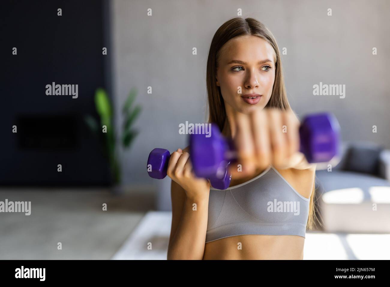 Sporty beautiful woman exercising with dumbbell at home to stay fit Stock Photo