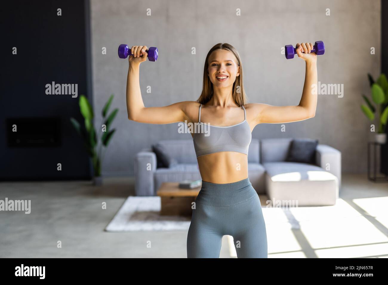 Sporty beautiful woman exercising with dumbbell at home to stay fit Stock Photo