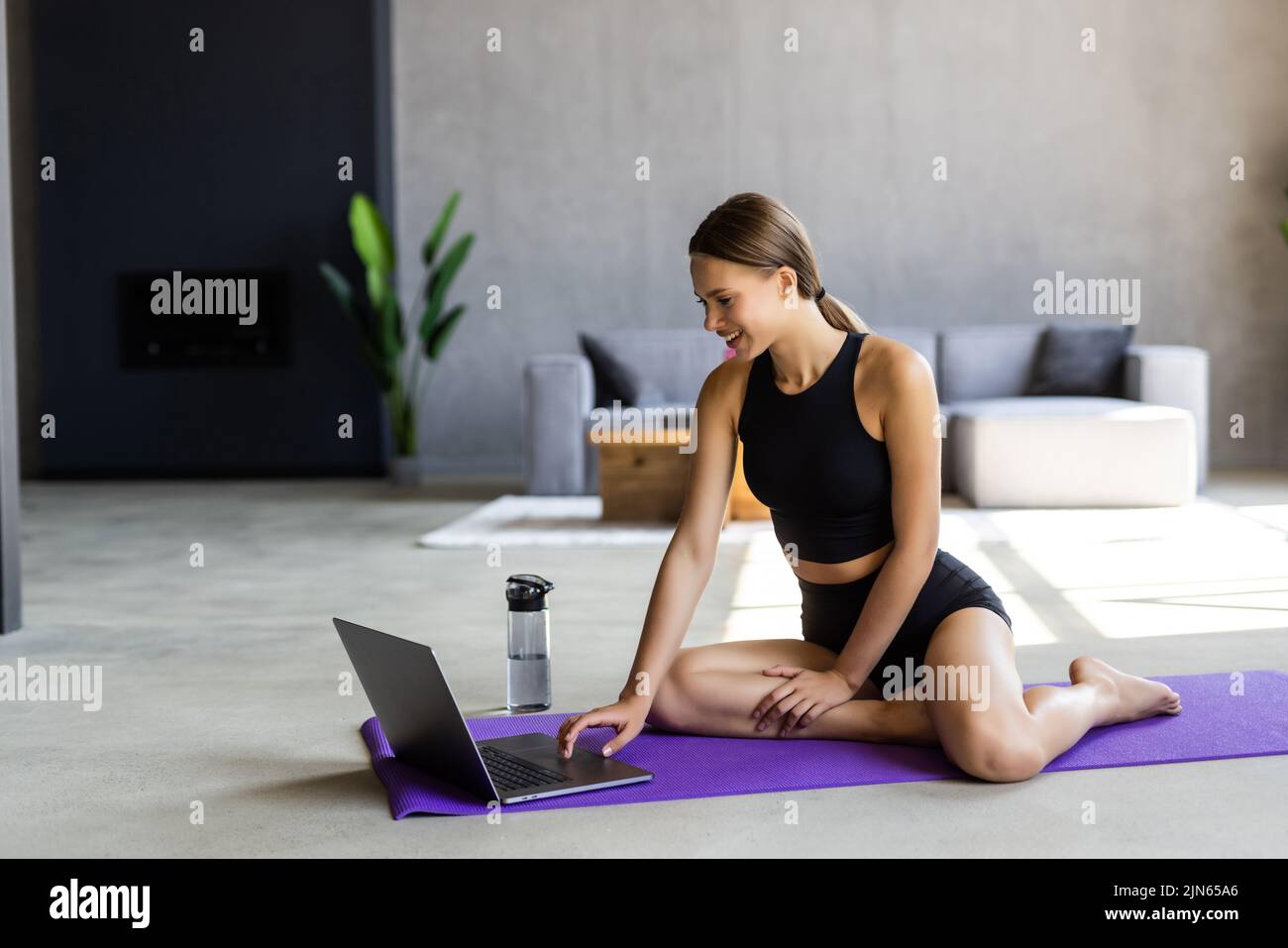 Sporty young brunette woman exercising with dumbbells at home, choosing lesson on laptop, watching fitness video on Internet or having online fitness Stock Photo