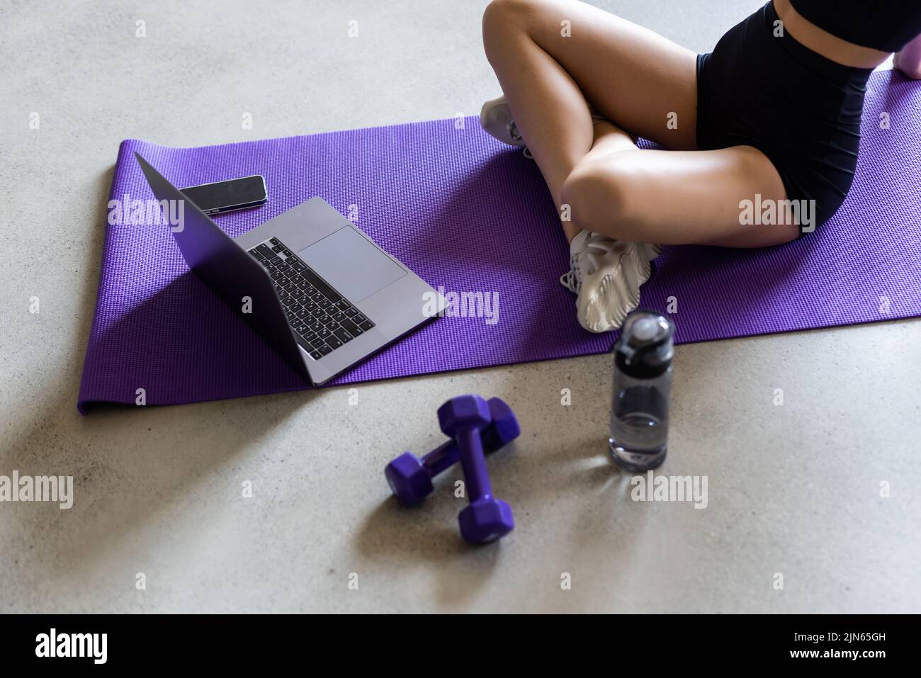 Close up body of woman doing yoga exercises on mat in front of laptop. Stock Photo