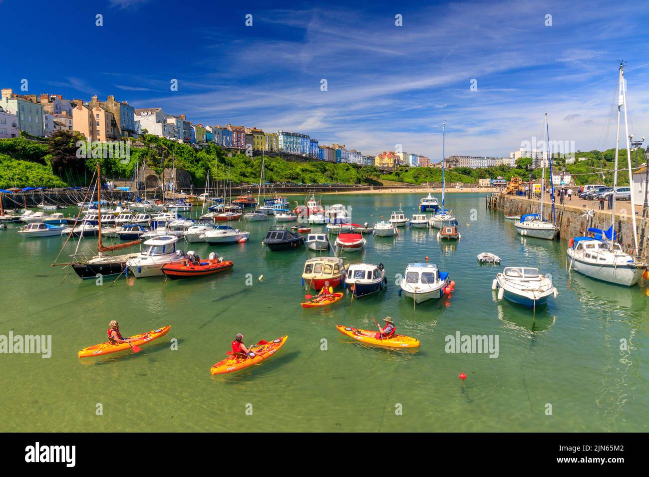 A group of sea kayakers in the picturesque sheltered harbour, overlooked by rows of colourful houses in Tenby, Pembrokeshire, Wales, UK Stock Photo