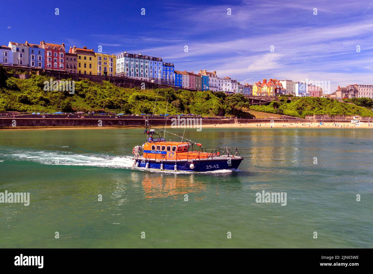 A decommissioned lifeboat drifts across the picturesque sheltered harbour, overlooked by rows of colourful houses in Tenby, Pembrokeshire, Wales, UK Stock Photo