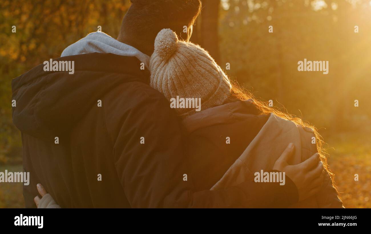 View from back close-up young couple in love in autumn park hugging cute chatting talking enjoying pleasant pastime together admiring view of sunset Stock Photo