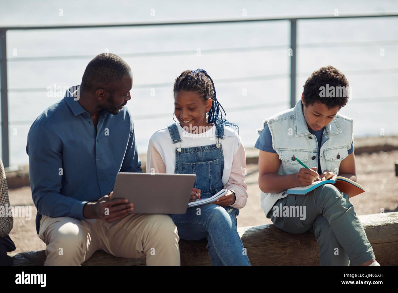 Group of smiling black kids with teacher using laptop together during outdoor lesson in Summer school Stock Photo