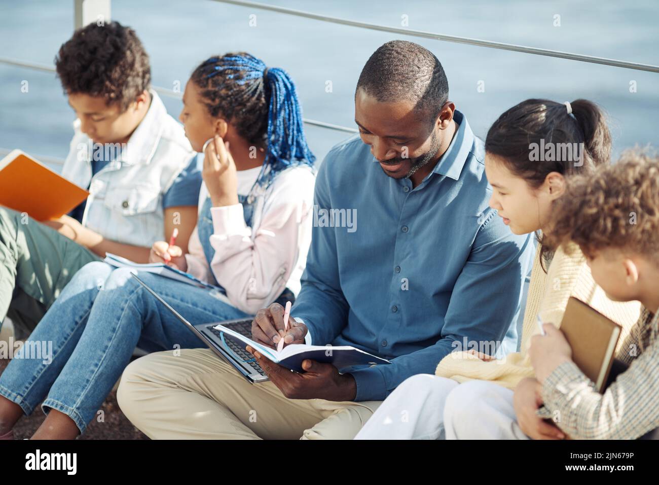Portrait of smiling male teacher with diverse group of children enjoying outdoor class in sunlight Stock Photo