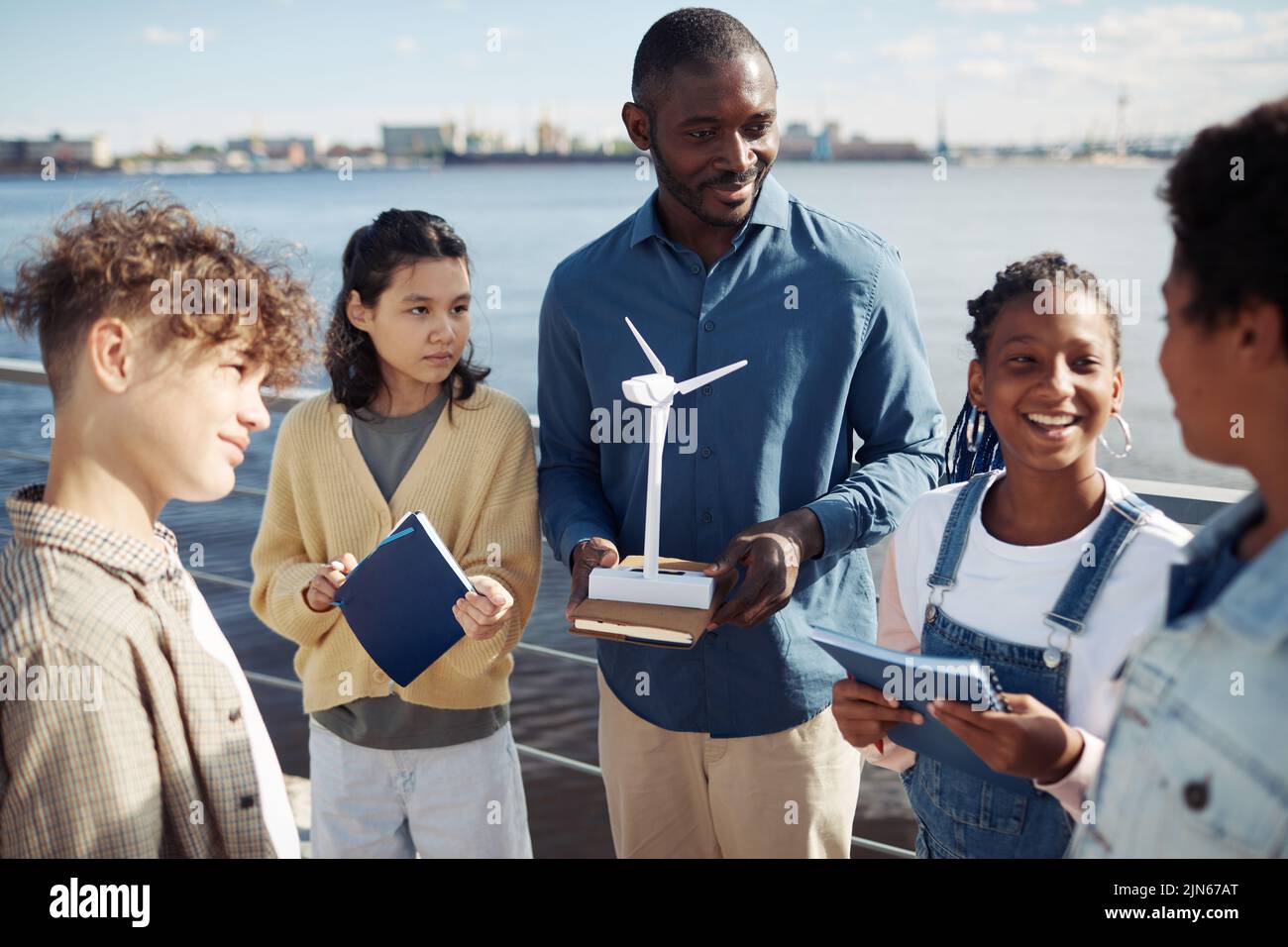 Portrait of black male teacher demonstrating wind mill model to group of kids during outdoor class in sunlight Stock Photo