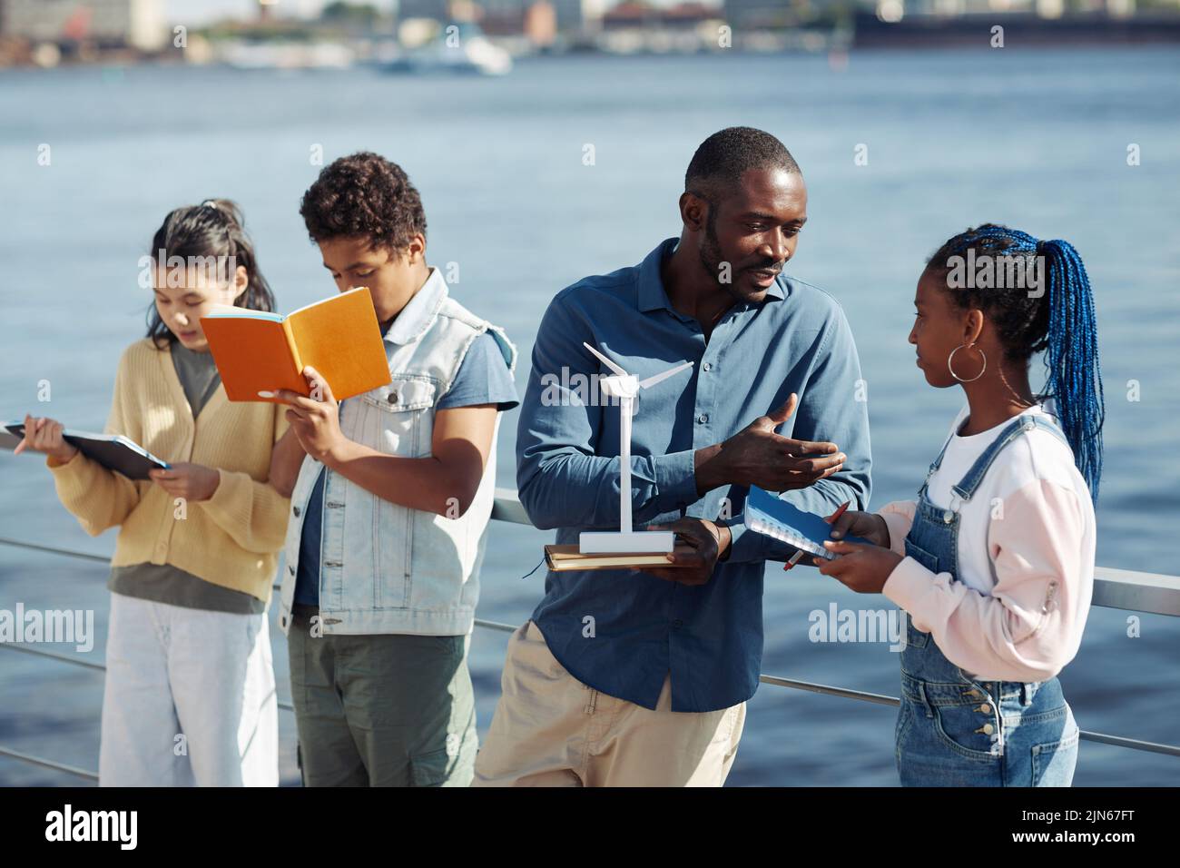 Portrait of black male teacher talking to teenage girl during outdoor class by water Stock Photo