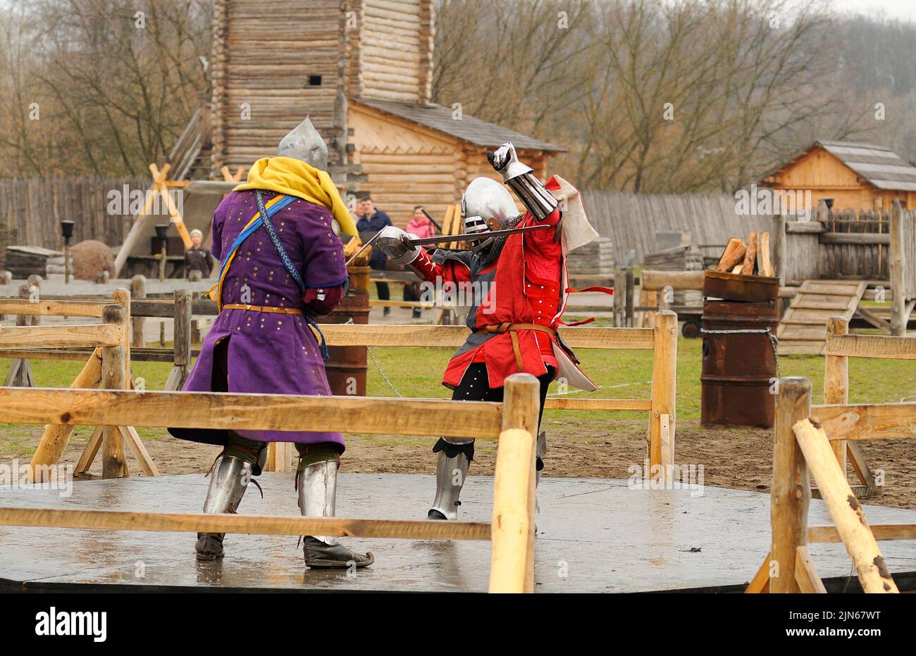 Men reenactors in metal armor of an Old Rus knights reconstructing sword fight, wooden fortress on a background. Kyiv Rus park, Ukraine Stock Photo