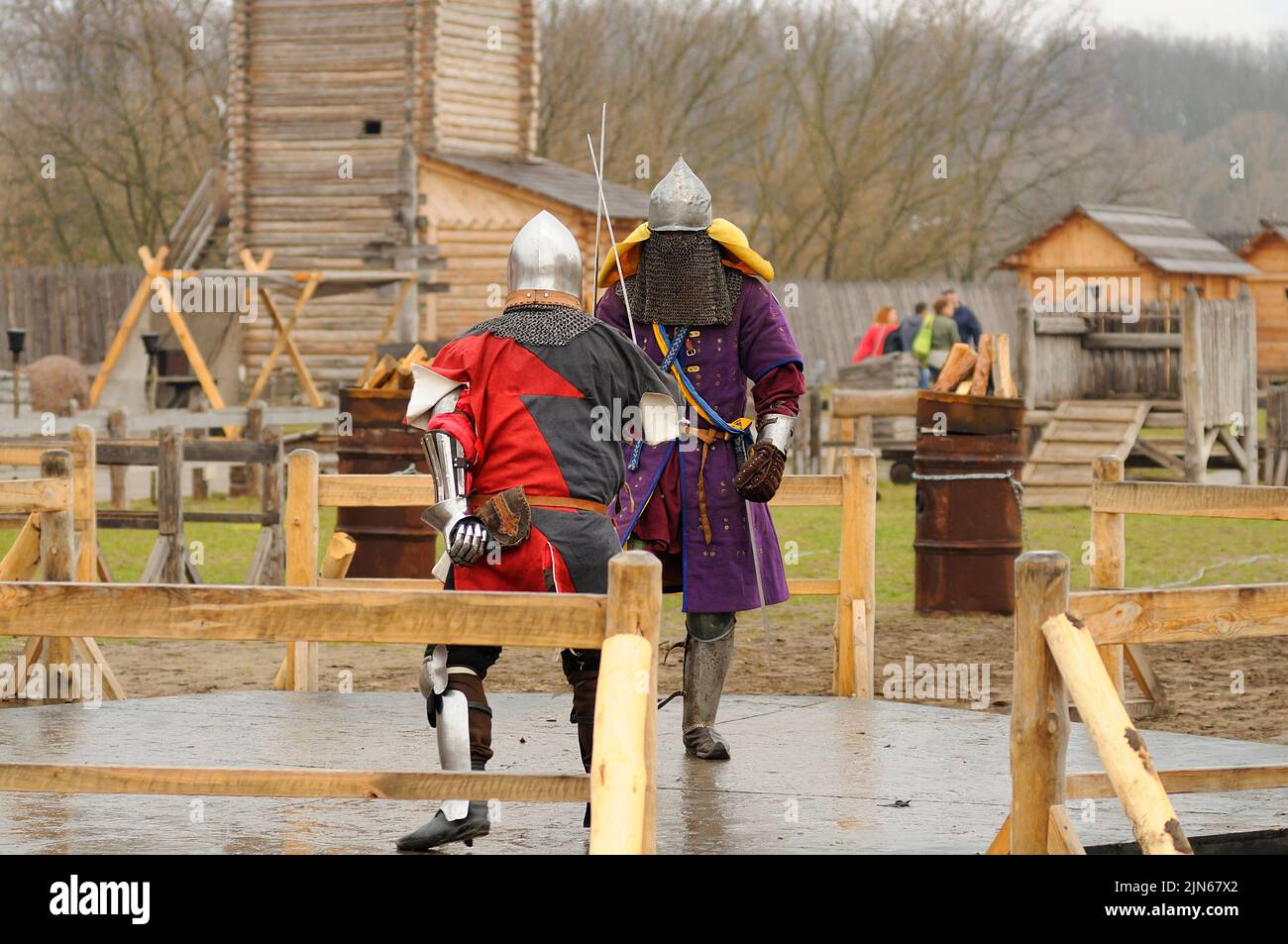 Men reenactors in metal armor of an Old Rus knights reconstructing sword fight, wooden fortress on a background. Kyiv Rus park, Ukraine Stock Photo