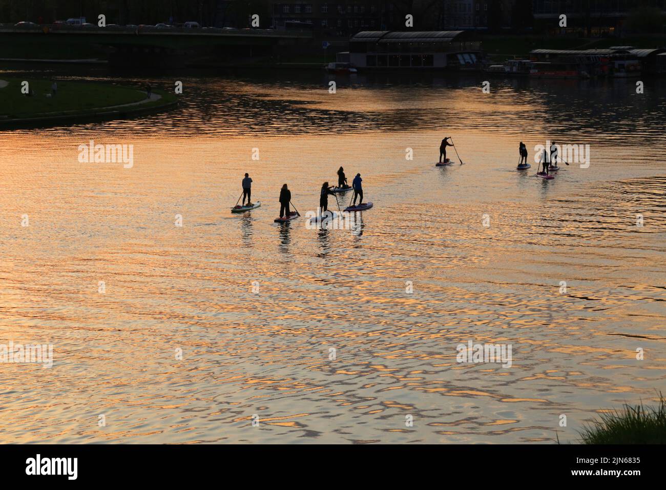Cracow. Krakow. Poland. Silhouettes of people sailing SUP boards on the river in the sunset light. Stock Photo