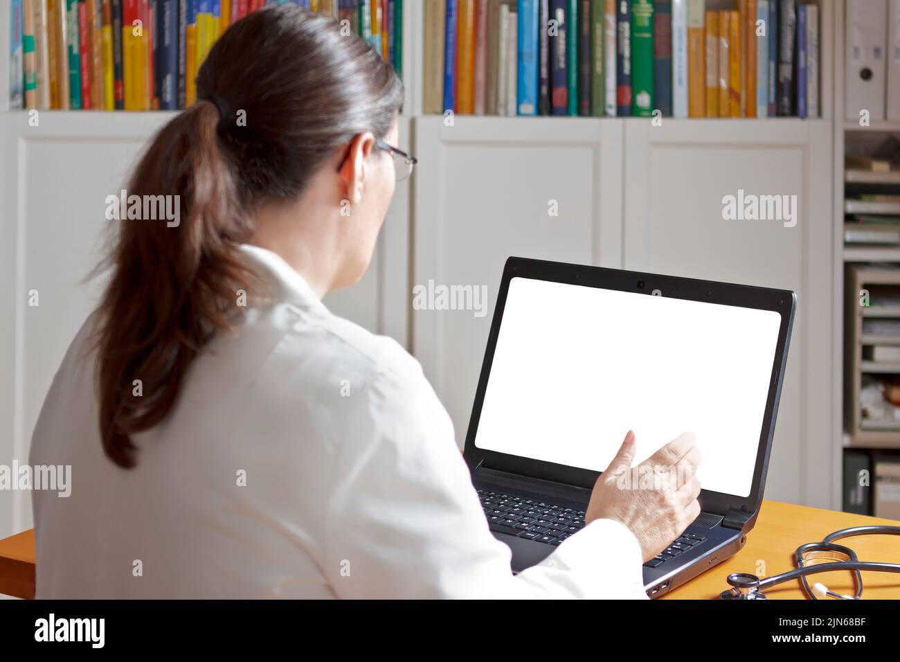 Telemedicine concept mock-up: female doctor or pharmacist talking in front of a laptop with a blank white screen. Stock Photo