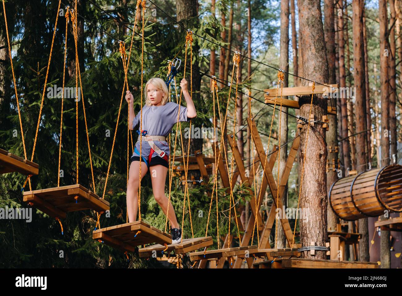 A girl passes an obstacle in a rope town. A girl in a forest rope park Stock Photo