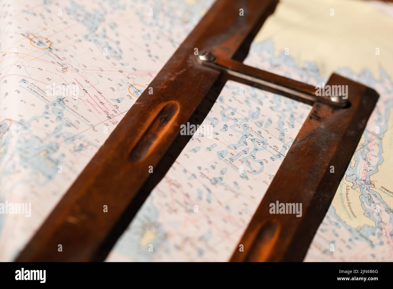 Vintage wooden parallel ruler lays on a nautical paper chart. It is a drafting instrument used by navigators to draw parallel lines on charts Stock Photo