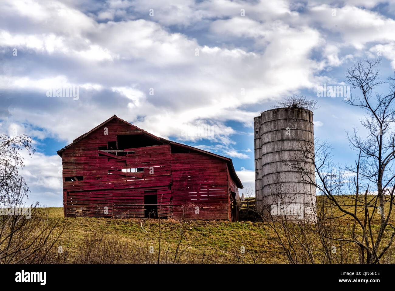 Weathered barn and silo with blue cloudy sky on a hill Stock Photo