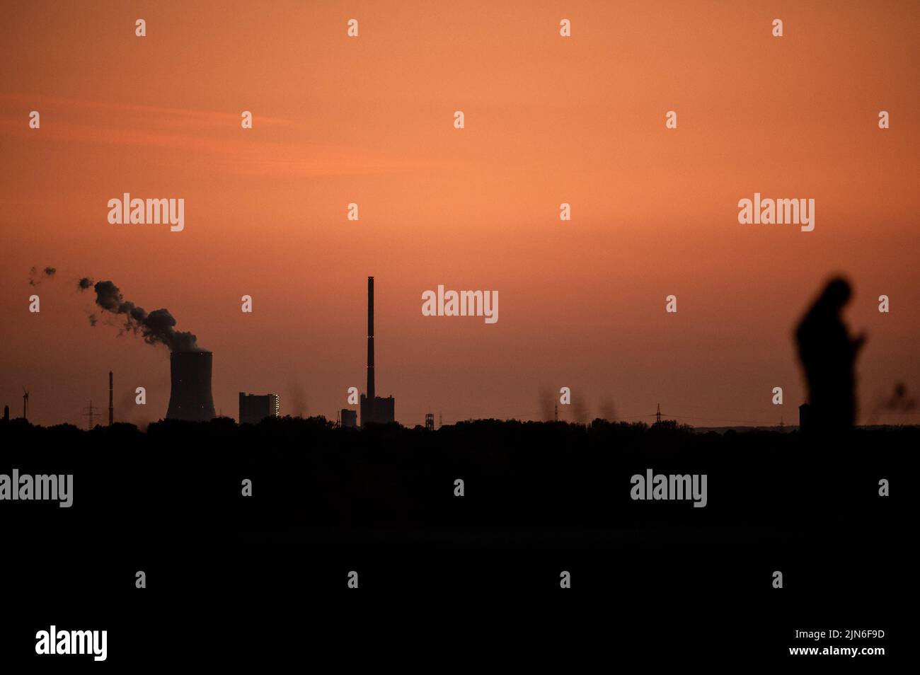Bottrop, Germany. 08th Aug, 2022. The Steag power plant in Duisburg Walsum can be seen at sunset while a person in the foreground is walking on the Tetraeder slag heap. Credit: Fabian Strauch/dpa/Alamy Live News Stock Photo