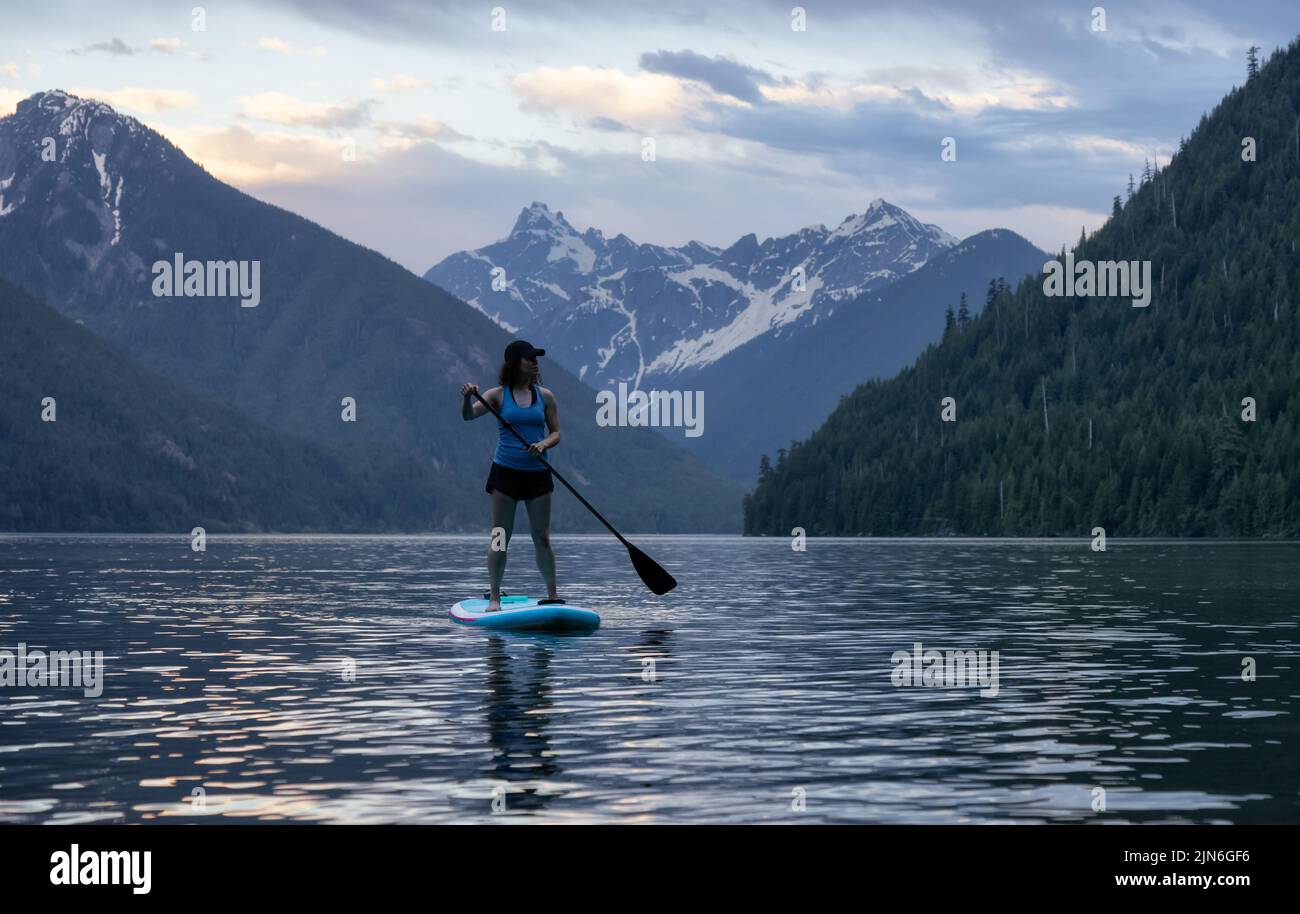 Adventurous Woman Paddle Boarding in a Lake around Canadian Mountain Landscape Stock Photo