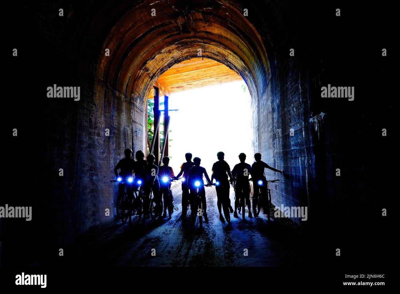 Group of people bikers biking through dark tunnel with headlights on Hiawatha Trail Stock Photo