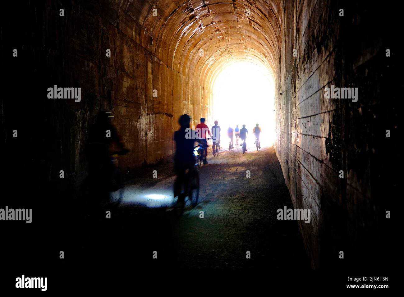 Group of people bikers biking through dark tunnel with headlights on Hiawatha Trail Stock Photo