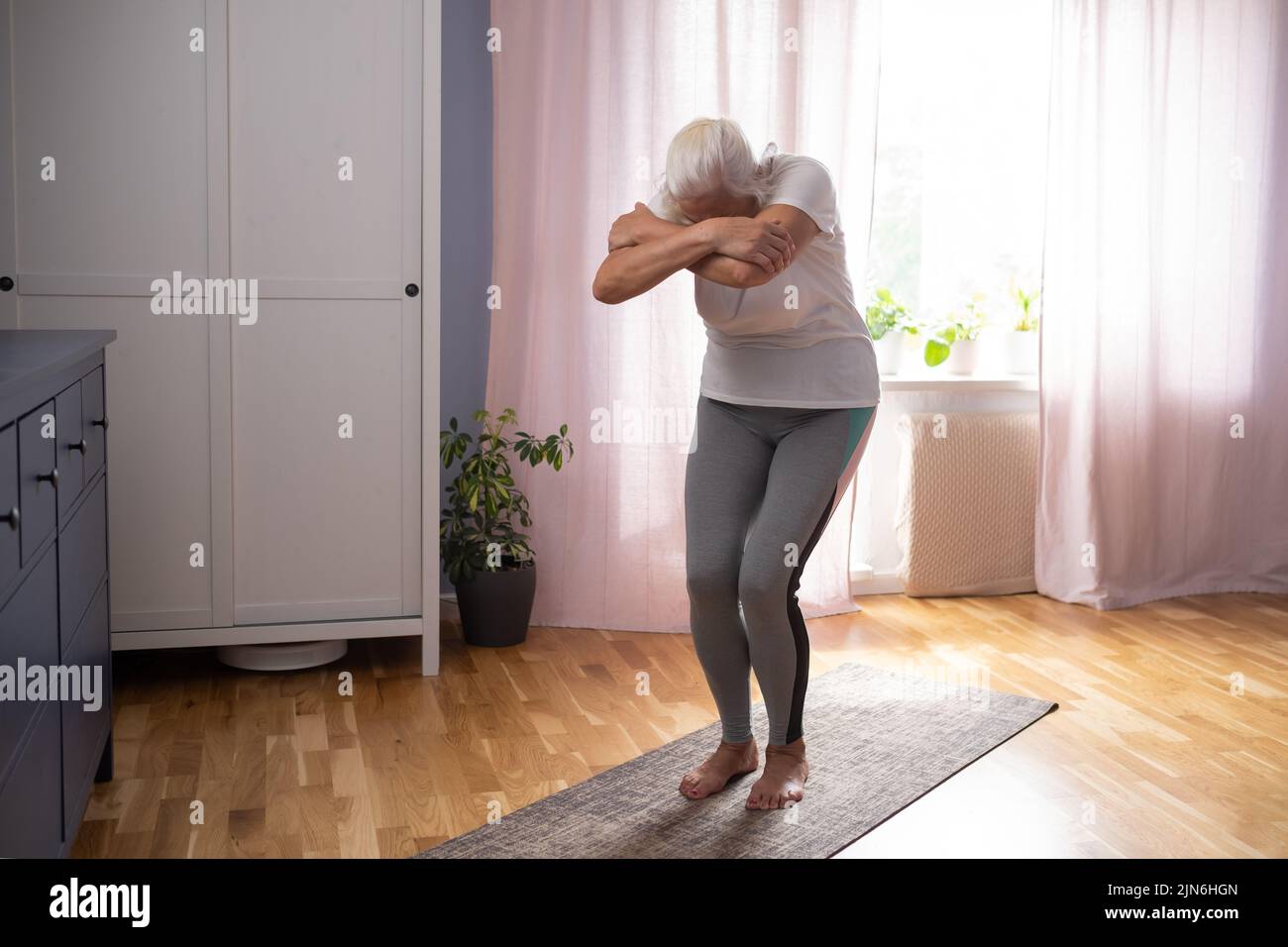 Senior woman working out indoors stretching muscles. Healthy lifestyle at old age. Stock Photo