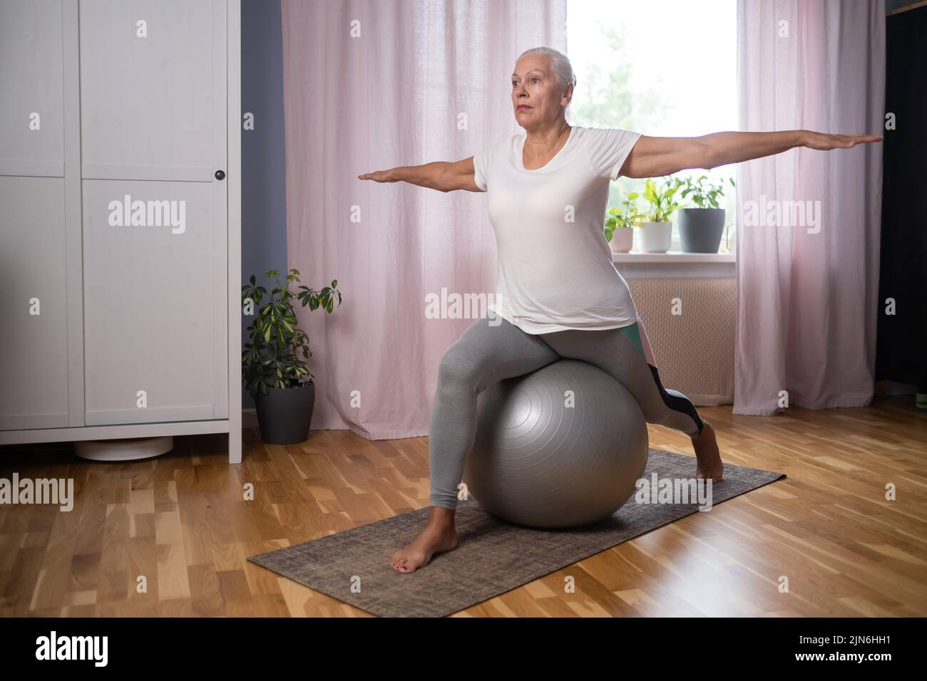 Happy senior lady doing yoga asana at living room. Stock Photo