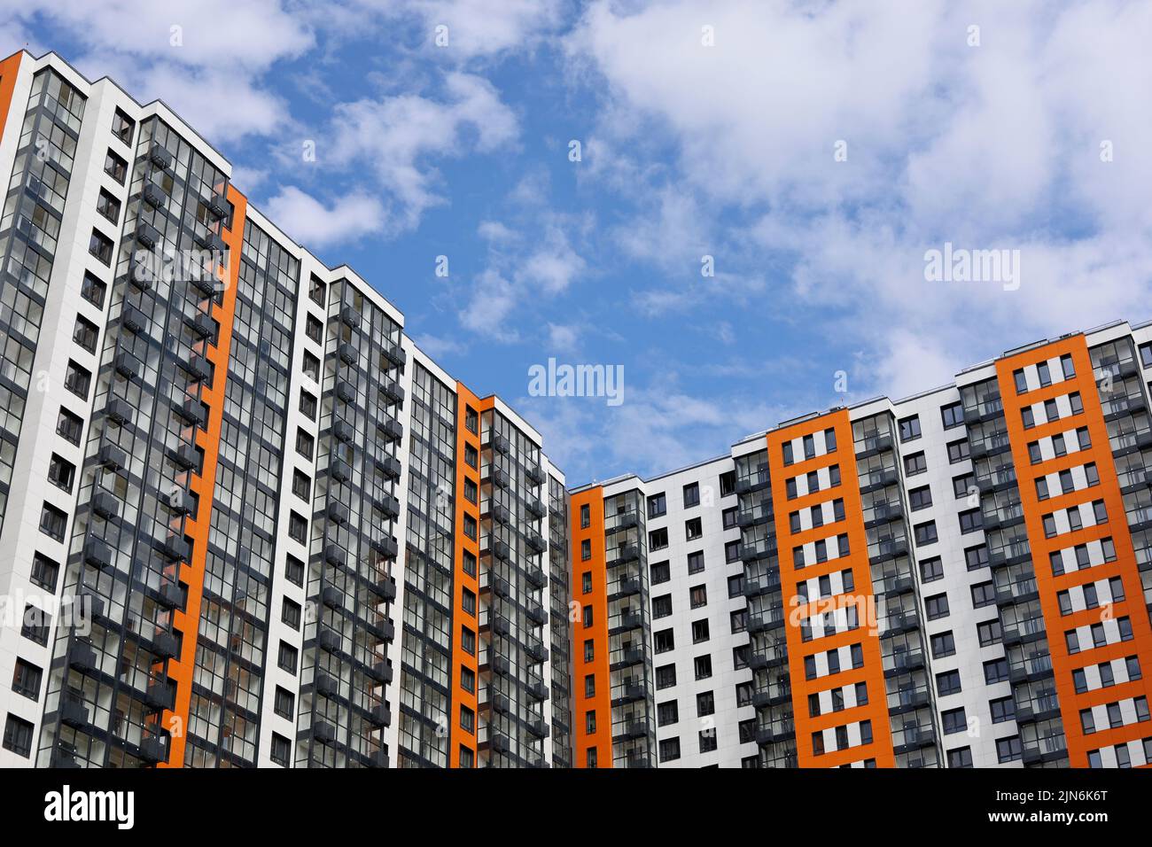 New residential building with orange and white cladding against blue sky with clouds. House with balconies and glazed loggias, high-rise construction Stock Photo