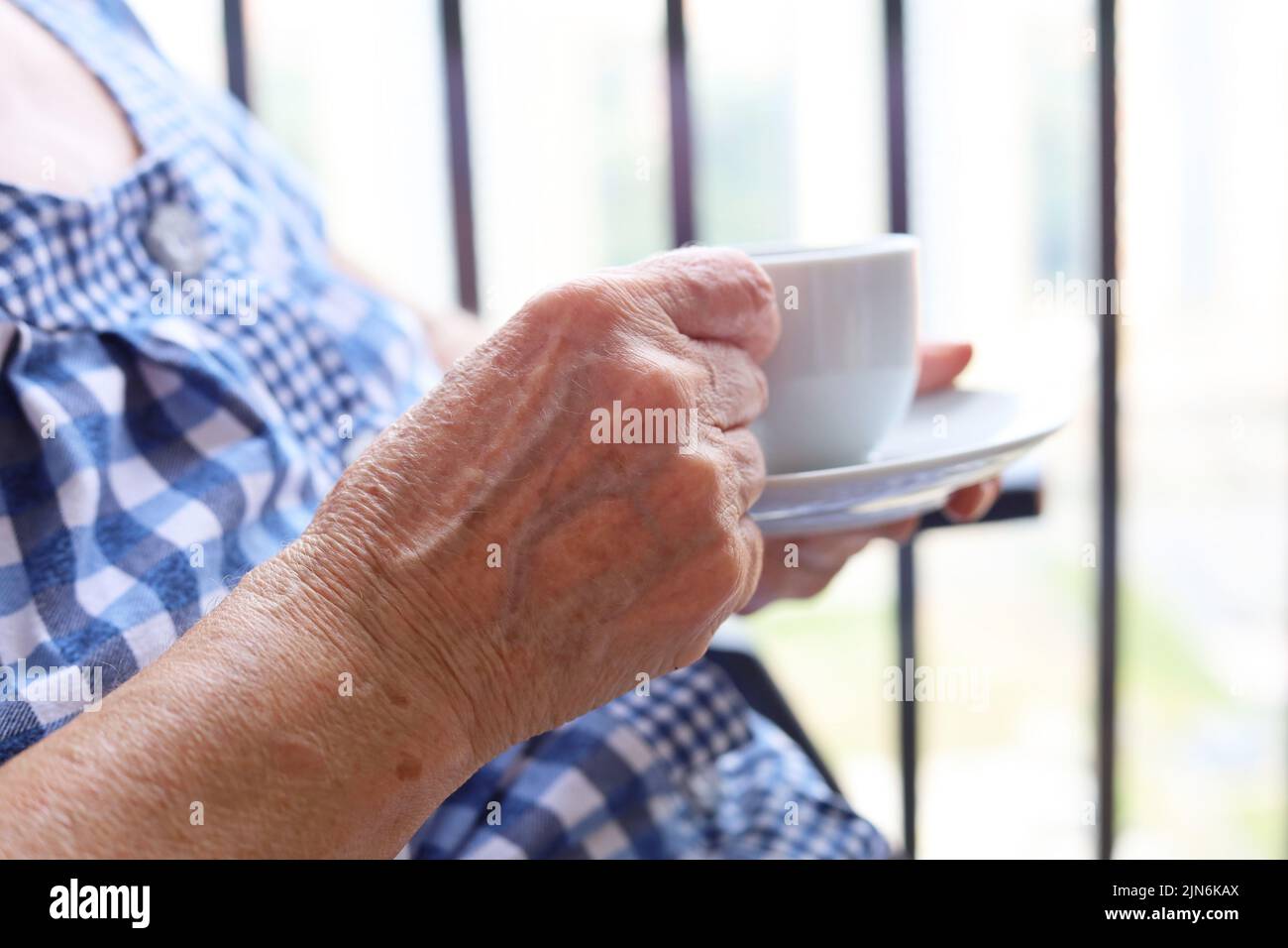 Elderly woman sitting with white cup of coffee in wrinkled hands. Concept of fresh morning, energy and enjoying life at retirement Stock Photo