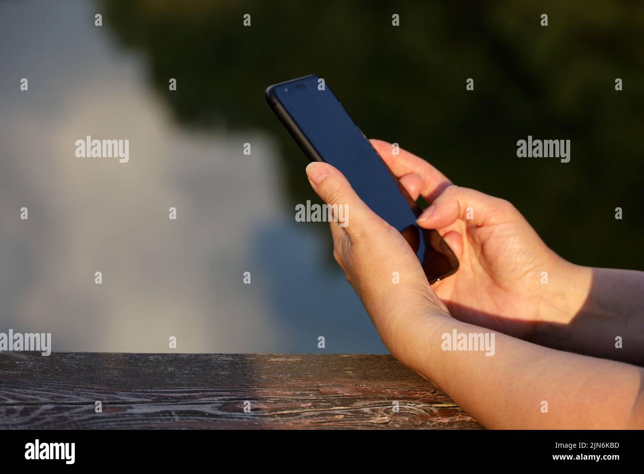 Female hands with smartphone close up on lake background. Woman using mobile phone in summer park Stock Photo