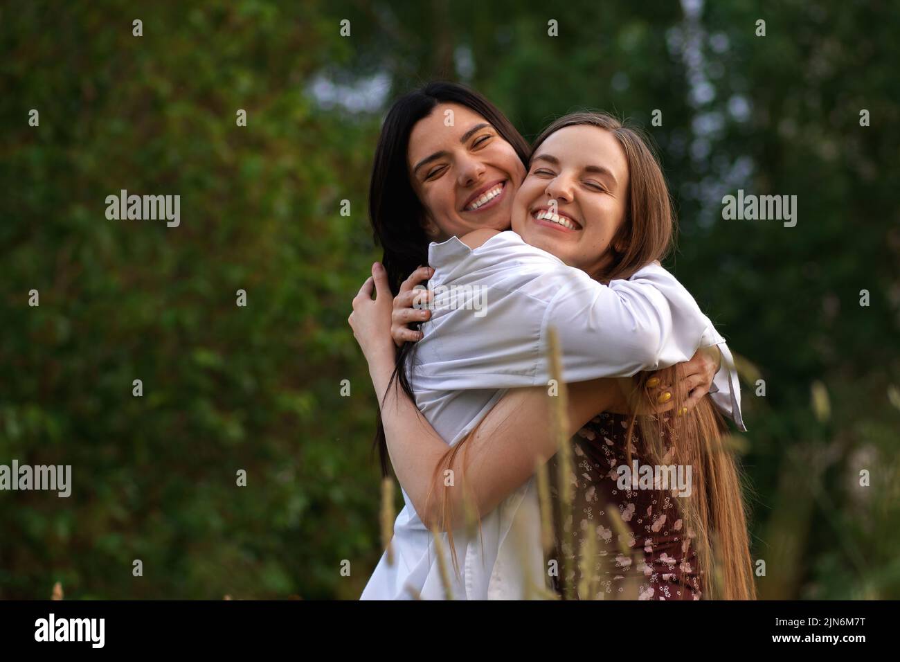 Two Girls with Long Hair Hugging Each Other and Laughing Stock Photo