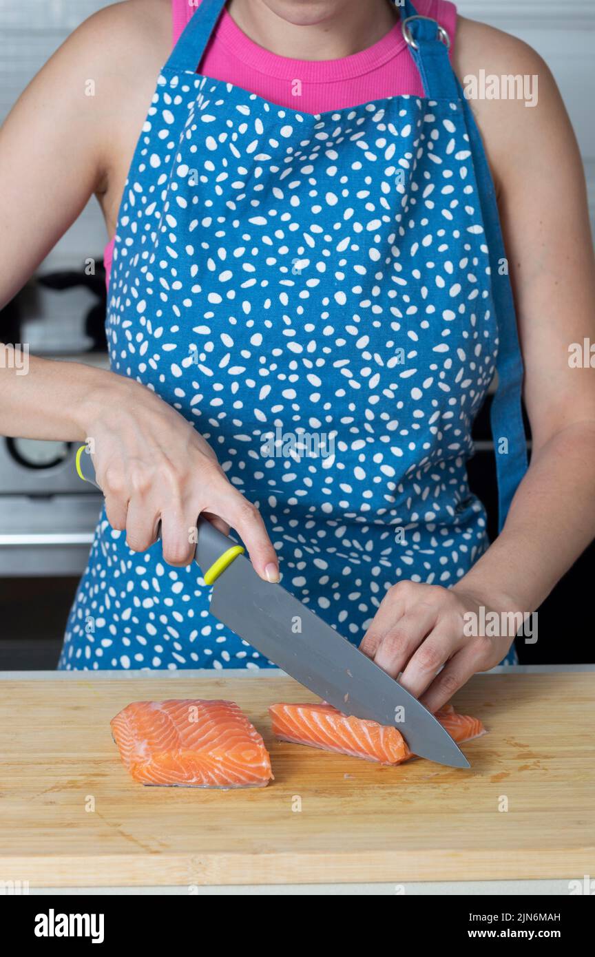 Woman cutting fresh salmon fillet on wooden plank vertical image Stock Photo
