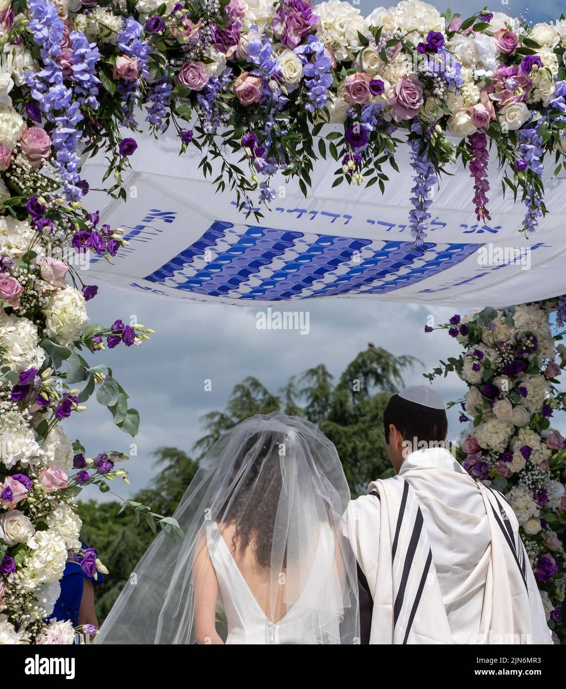 Jewish couple at marriage ceremony under a floral chuppa wedding canopy
