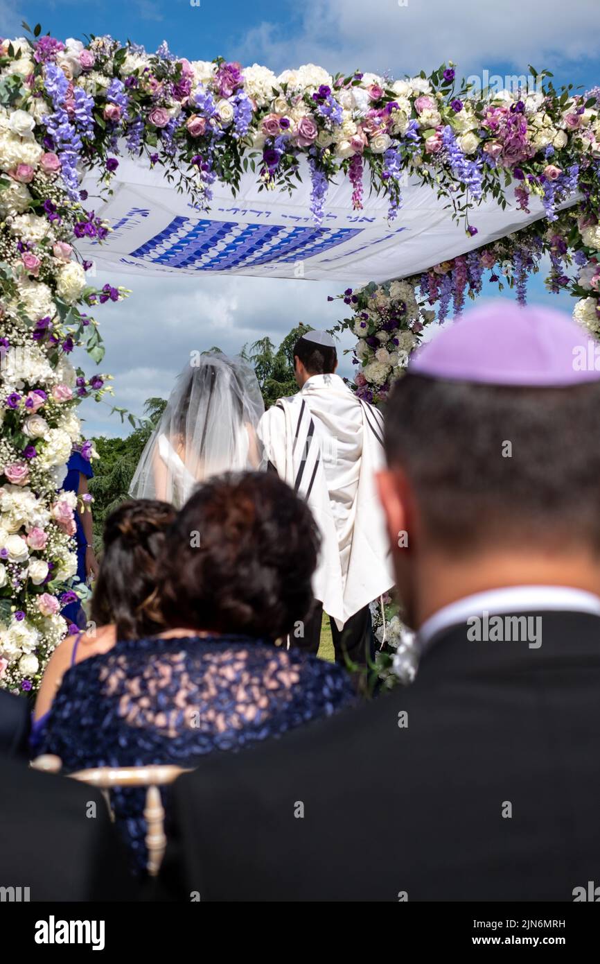 Jewish couple at marriage ceremony under a floral chuppa wedding canopy