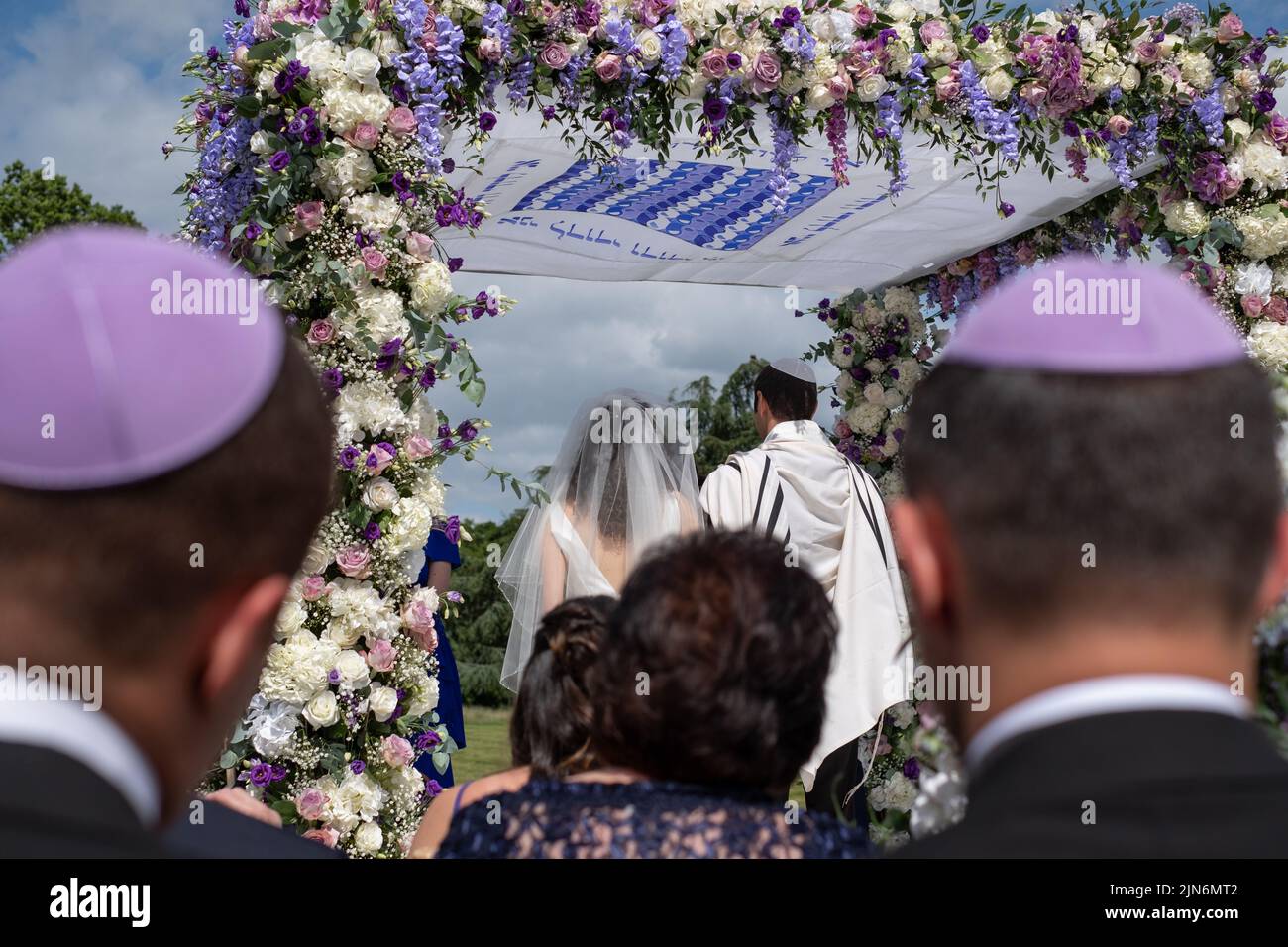 Jewish couple at marriage ceremony under a floral chuppa wedding canopy