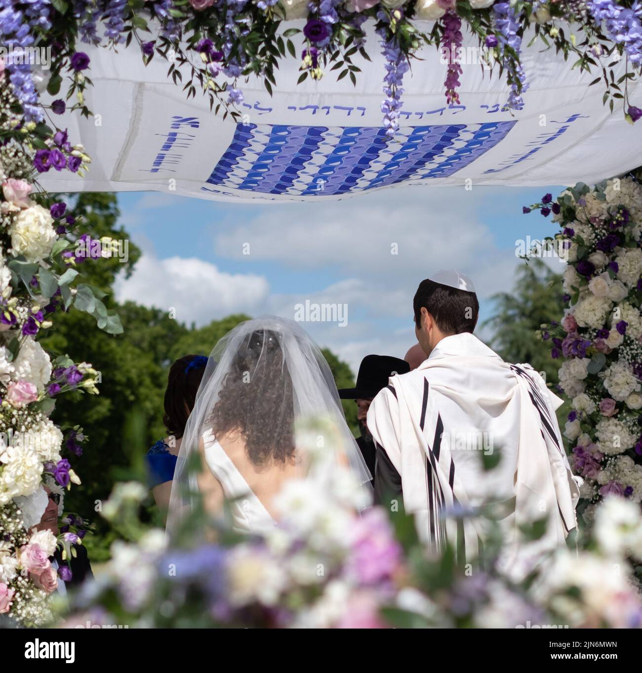 Jewish couple at marriage ceremony under a floral chuppa wedding canopy